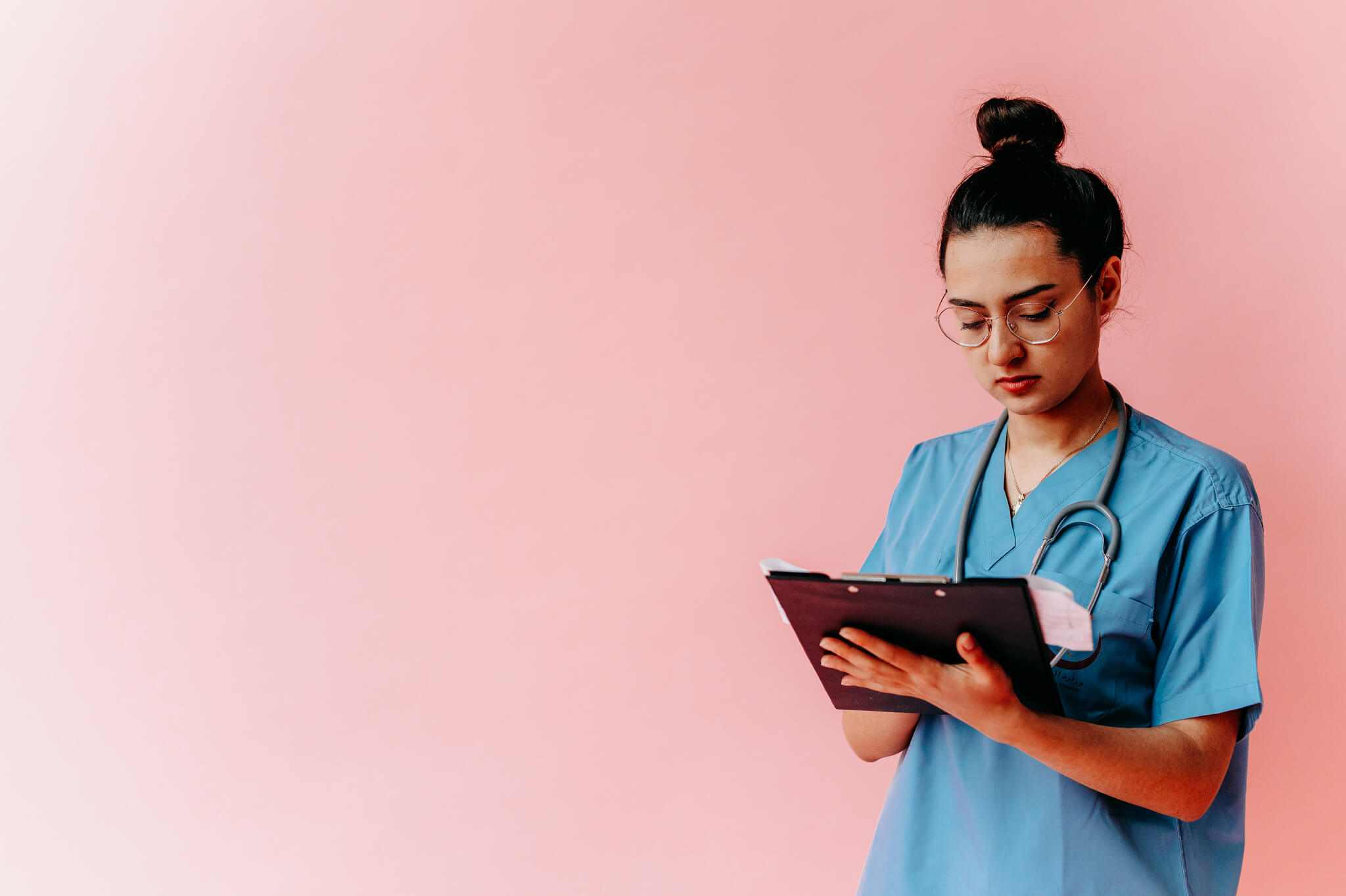 Medical resident standing while looking down at a clipboard with pink background