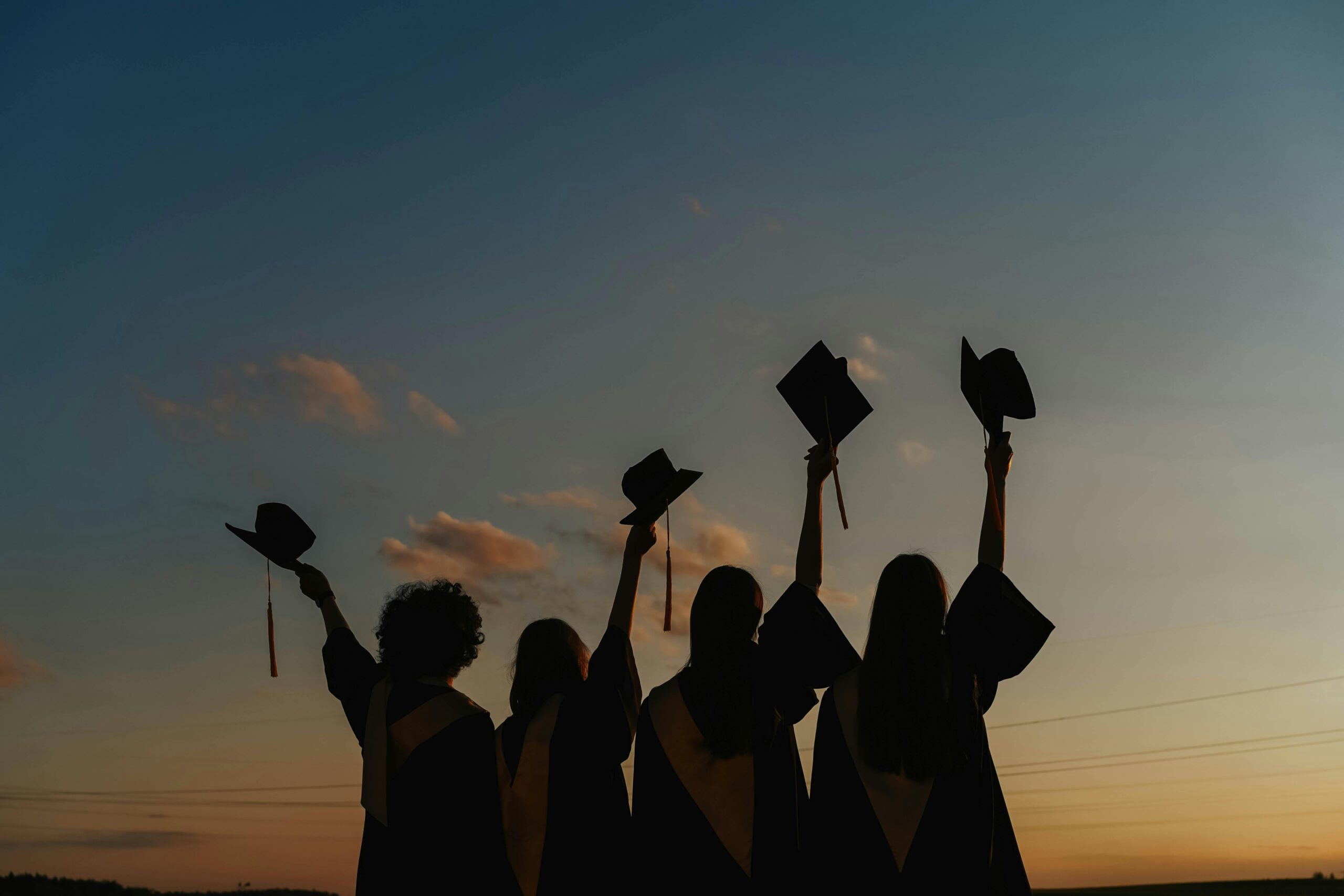 Four med school graduates silhouettes against a sunset sky